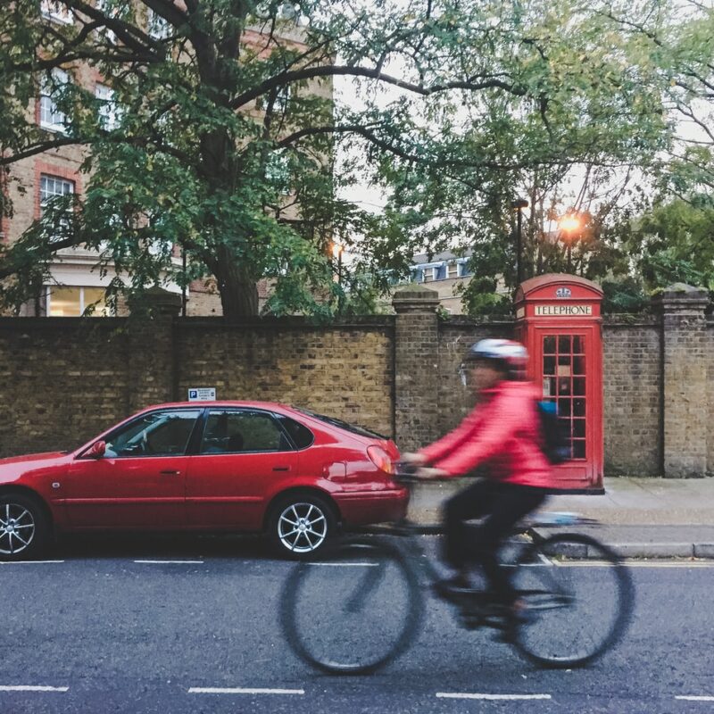 Woman cycling on road next to telephone box and car