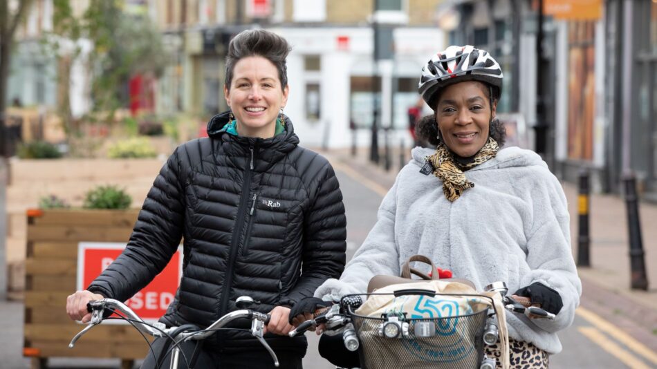 A pair of women smiling with their bikes and looking at the camera. This is one of our Cycle Buddies helping a new cyclist learn a route.