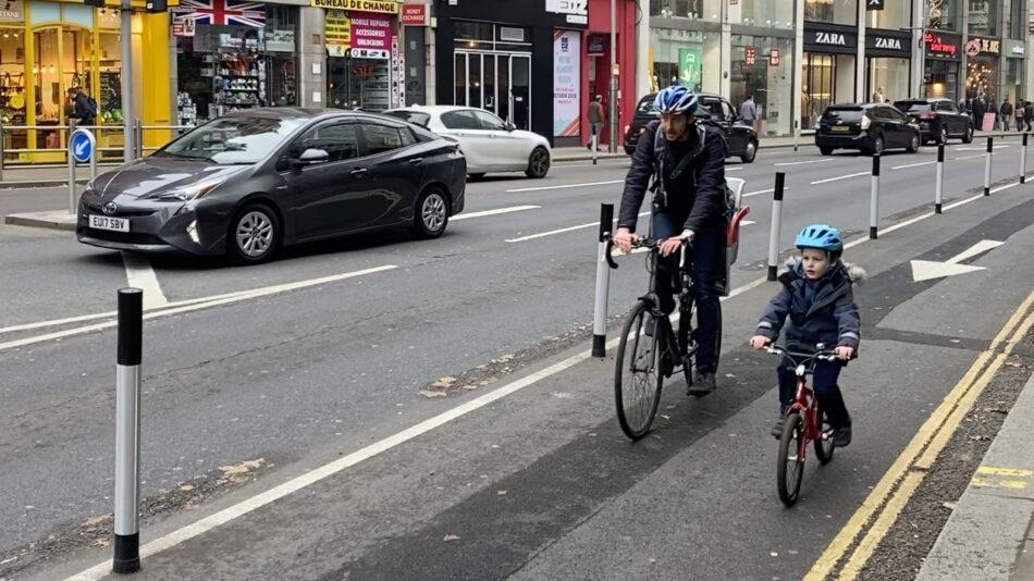 A father and son using a temporary cycle lane, marked off by wants, on Kensington High Street
