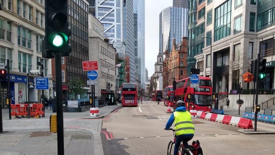 Person cycling in central London with big buildings and buses