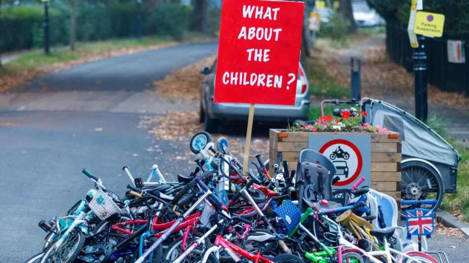 A big pile of discarded kids' bikes and scooters with a placard that says 'What About the Children?'