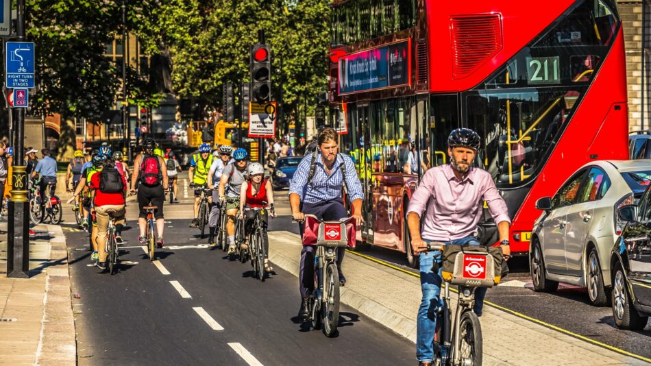 People cycling in a cycle lane (cycle superhighway) with a red double decker London bus in background