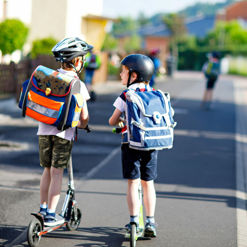 Two children on scooters with school rucksacks