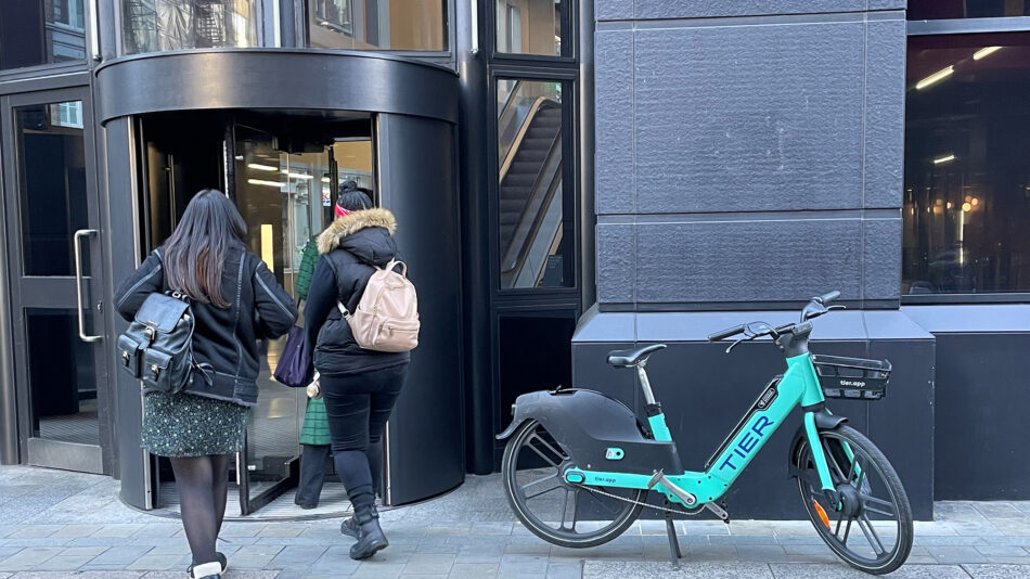 Blue-green dockless hire bike parked in front of a building