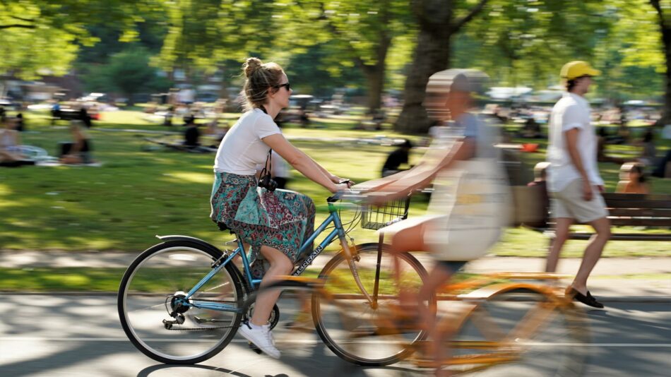 Woman on yellow bike cycling through park in sunshine