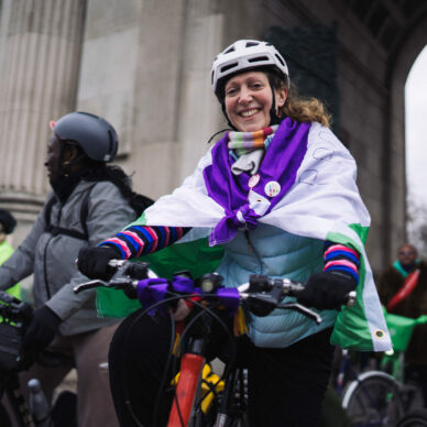 Woman on a bike dressed in suffragette colours - purple, white and green